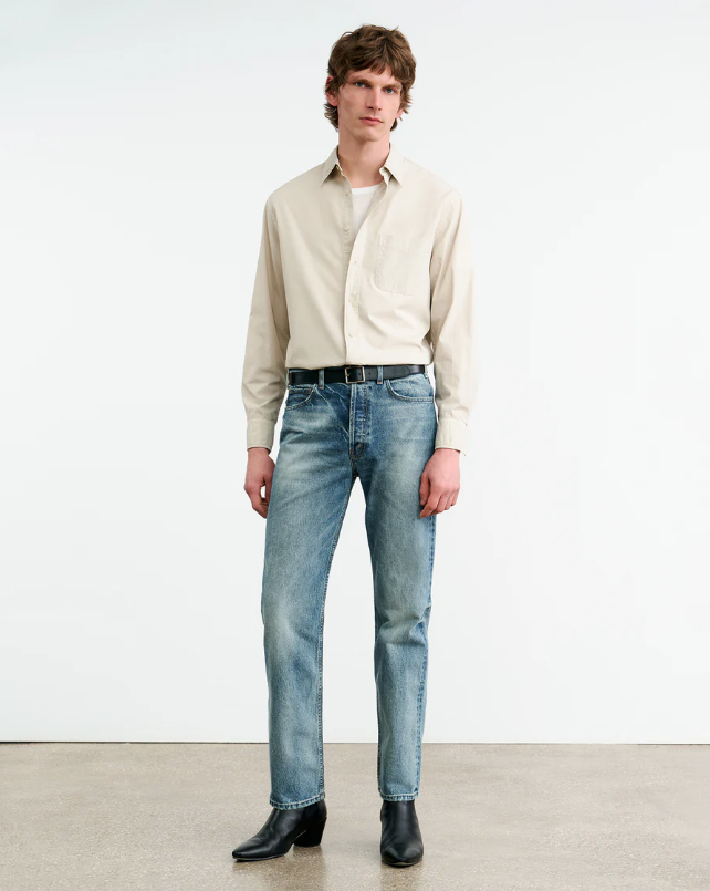 Man wearing a beige shirt and light blue jeans against a white background