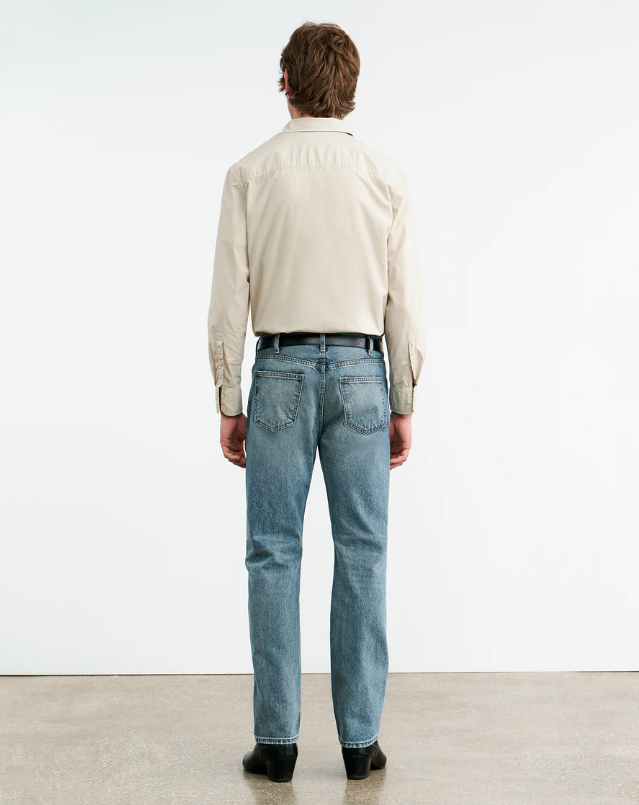 Person wearing a light-colored shirt and blue jeans standing against a white background