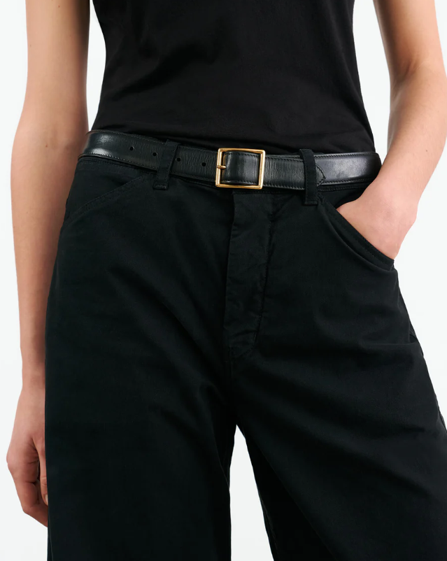 Person wearing black pants with a gold belt buckle on a white background