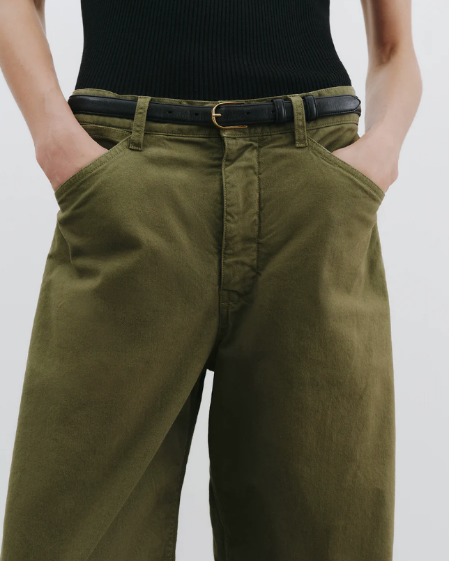 Person wearing olive green pants with a black belt on a plain background