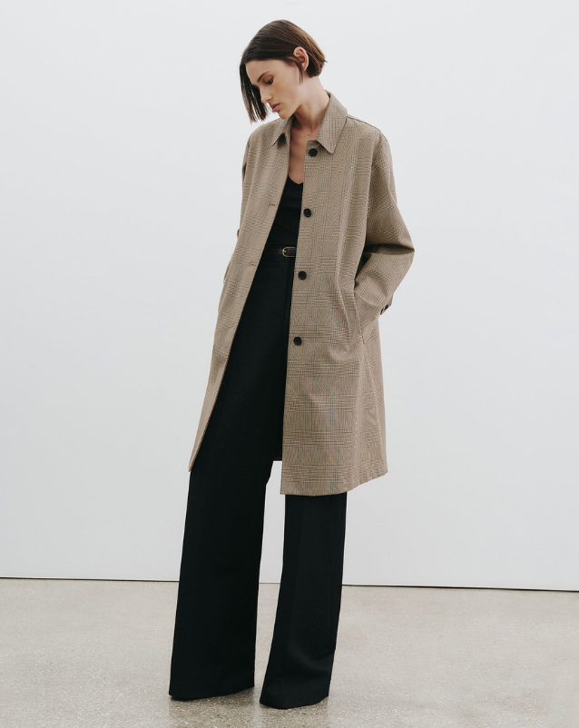 Person wearing a beige coat over a black dress with wide-leg pants against a white background