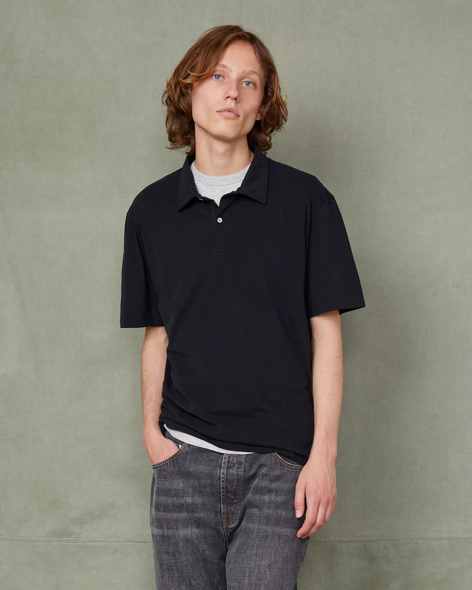 Person wearing a black polo shirt and jeans against a green background