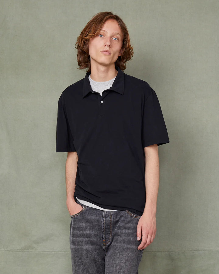 Person wearing a black polo shirt and jeans against a green background