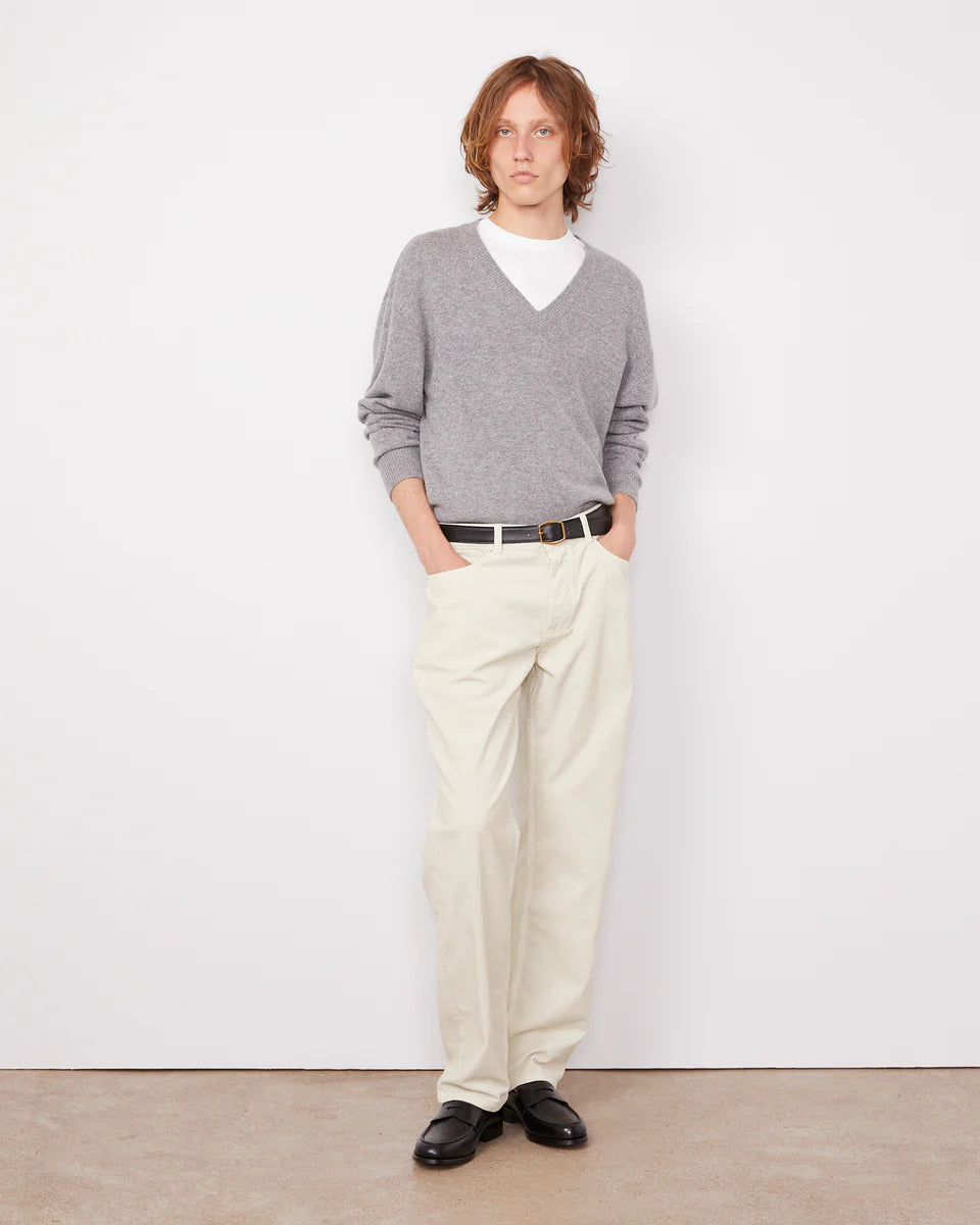 Person wearing a gray sweater, white shirt, beige pants, and black shoes against a white background
