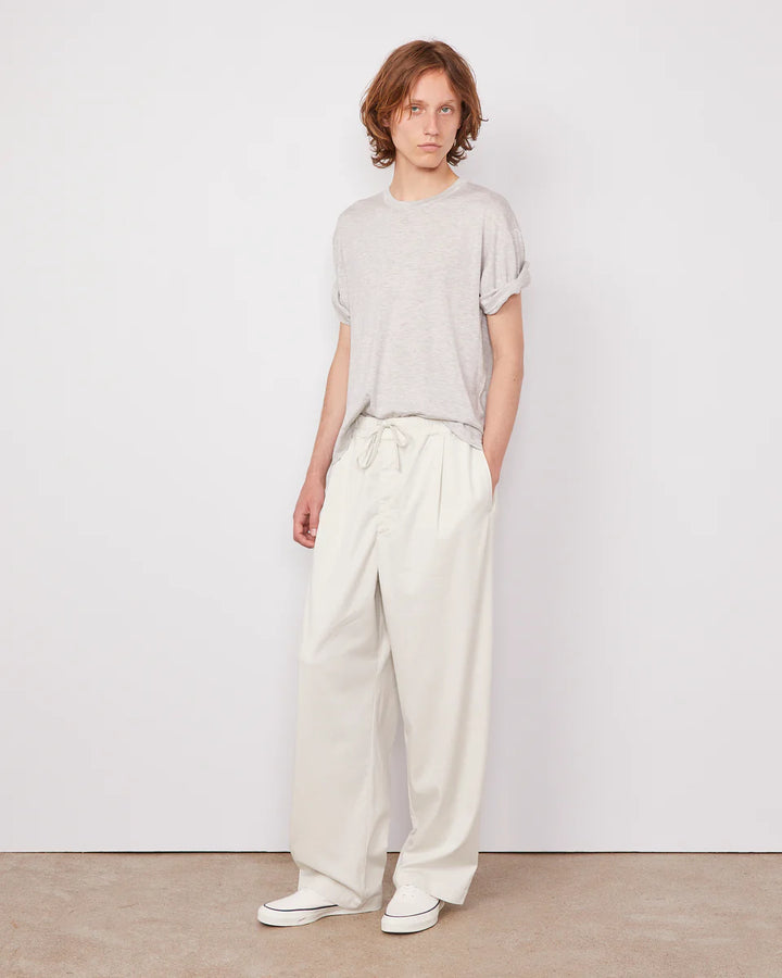 Person wearing a light gray t-shirt and white pants against a plain white background