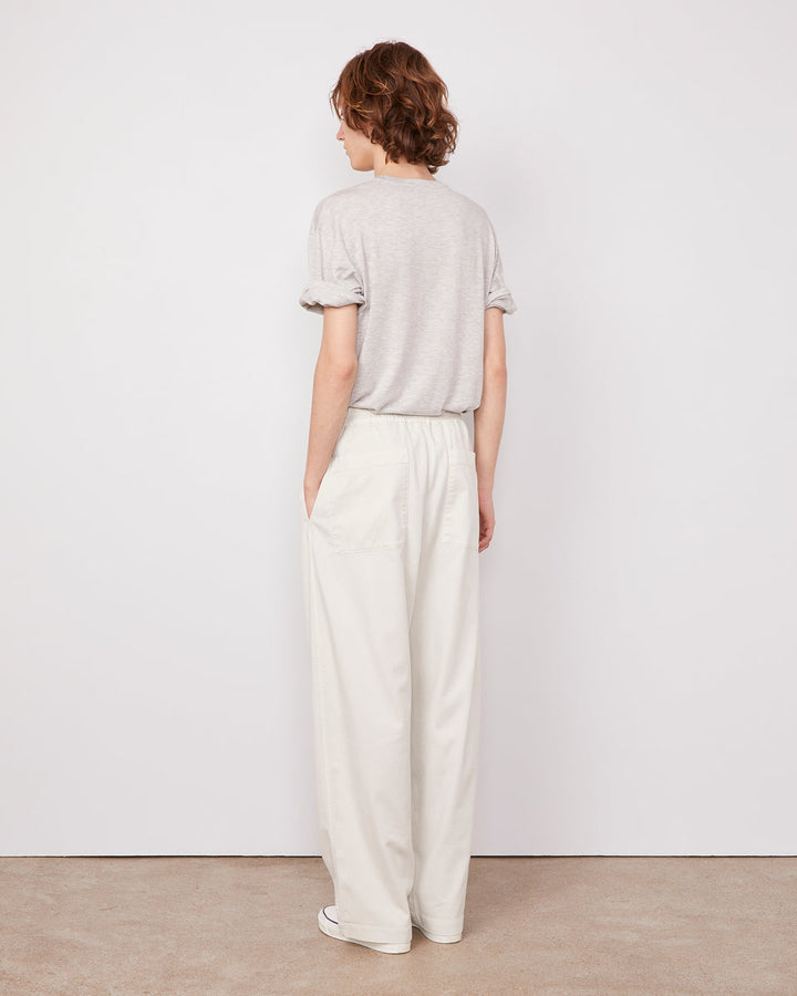 Person wearing a light gray top and white pants against a plain white background