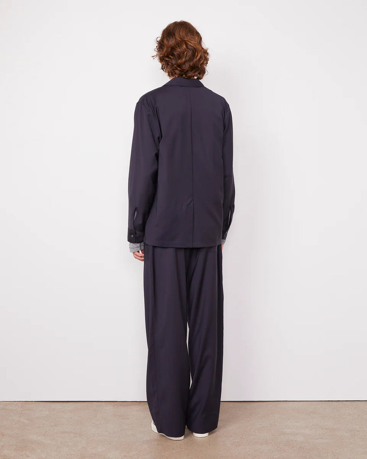 Person wearing a navy blue outfit standing against a white wall.