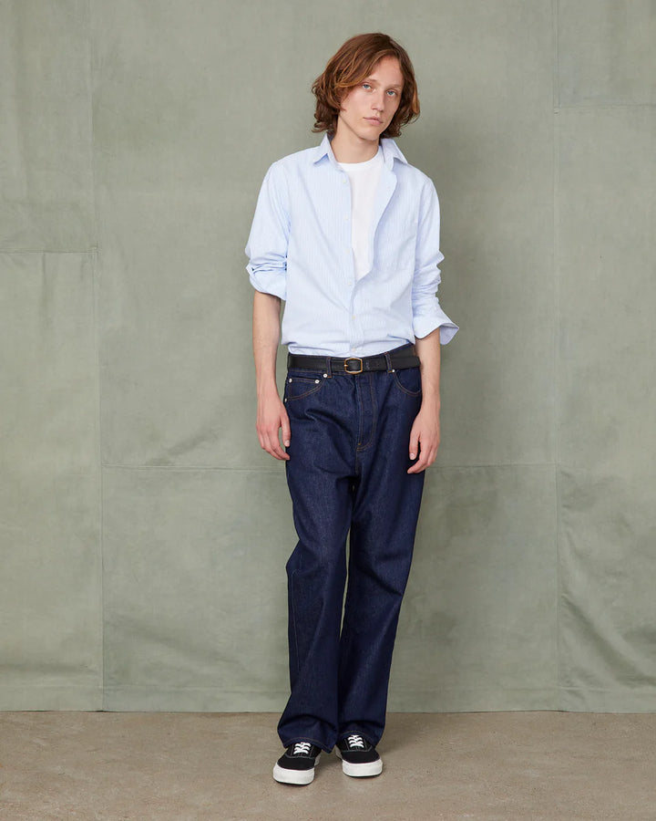 Person wearing a light blue shirt and dark blue pants against a plain background