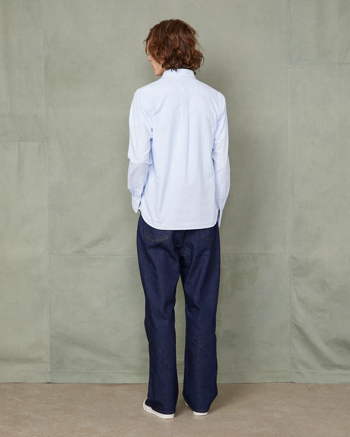 Person wearing a light blue striped shirt and dark blue pants against a plain background