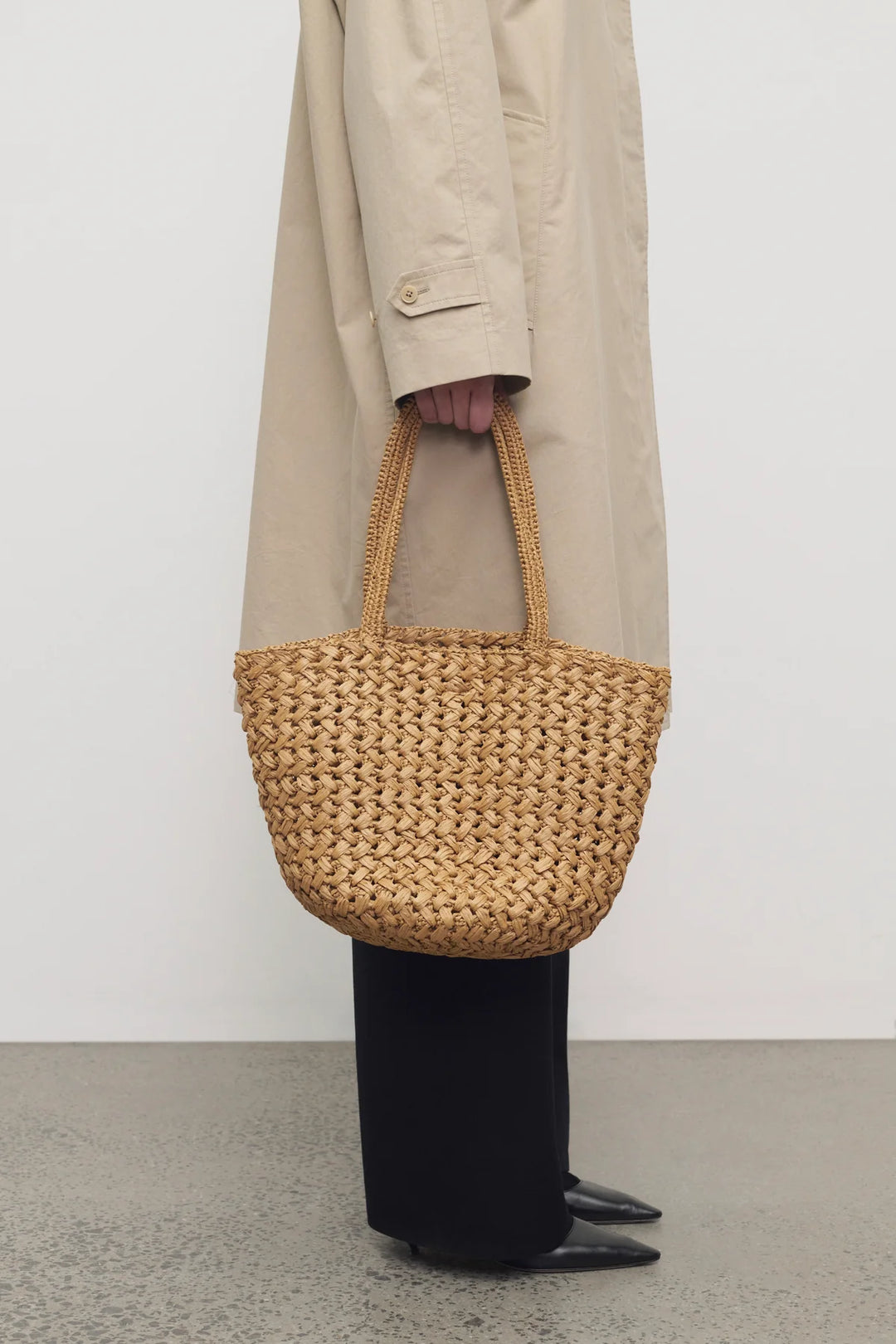 Person holding a woven handbag against a plain background