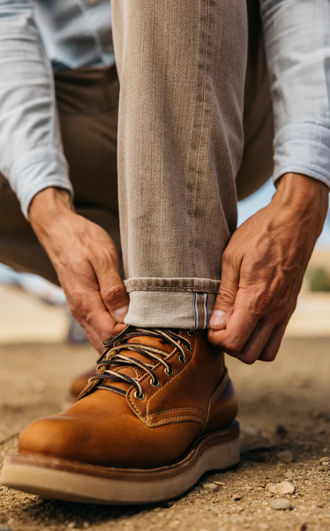 Person tying a brown leather boot outdoors