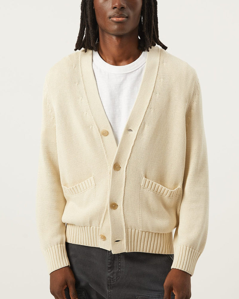 Person wearing a beige cardigan over a white shirt on a light gray background