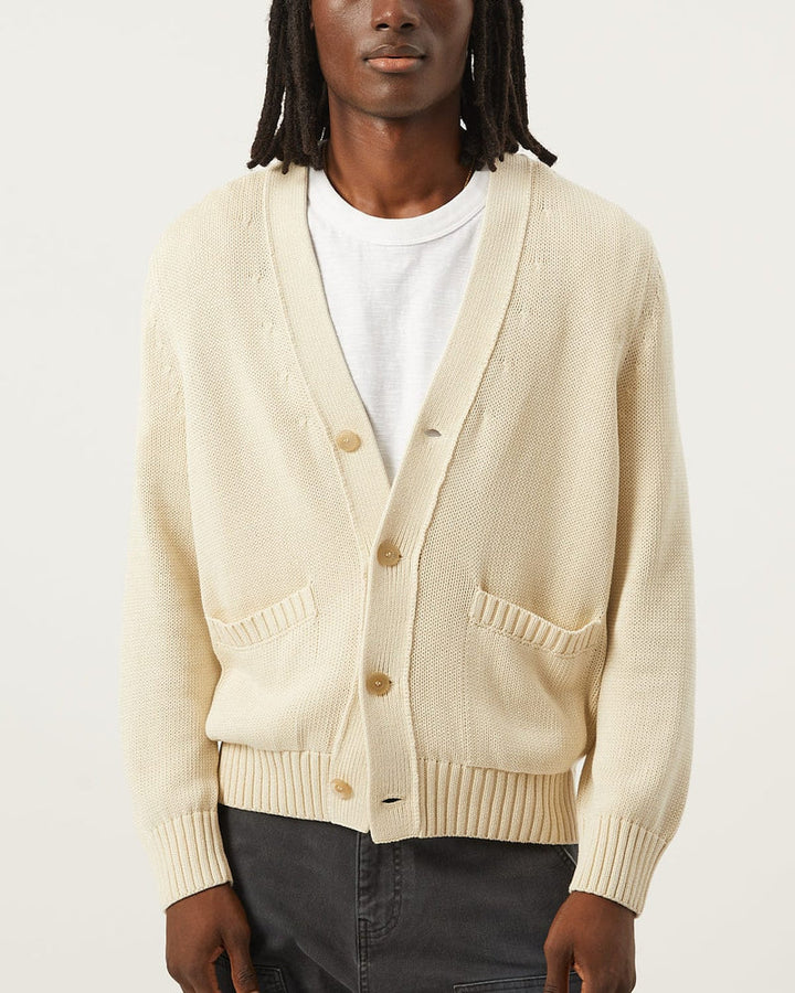 Person wearing a beige cardigan over a white shirt on a light gray background