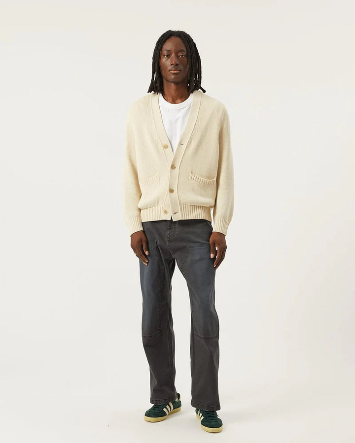 Person wearing a beige cardigan, white shirt, dark pants, and green shoes on a white background