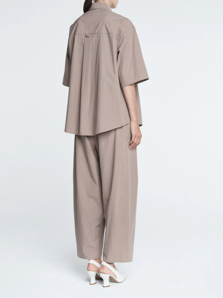 Person wearing a beige outfit with a shirt and pants on a white background