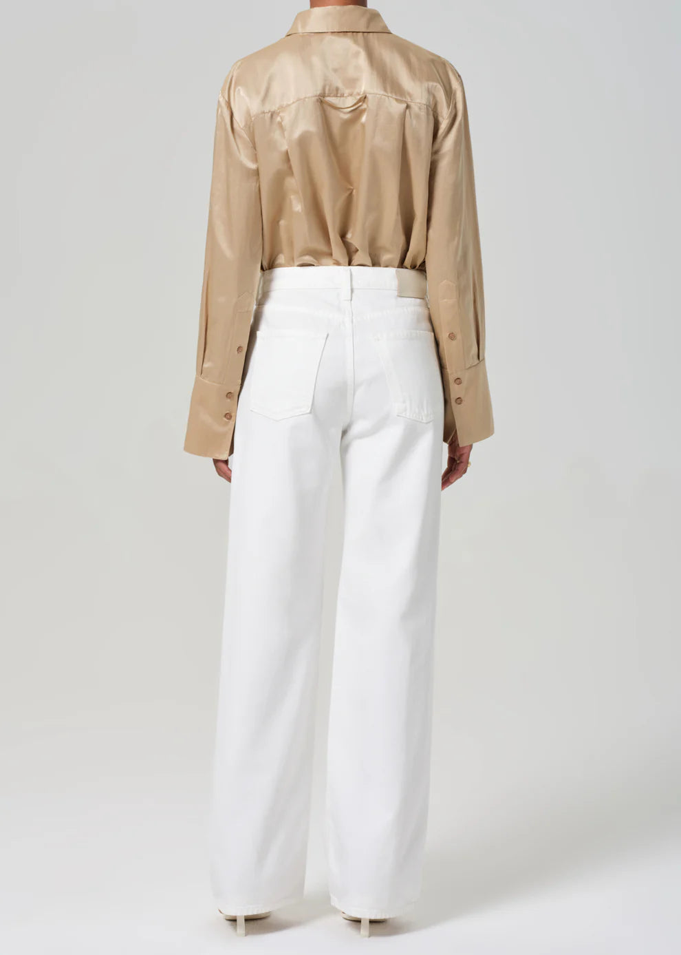 Person wearing a beige shirt and white pants on a plain background