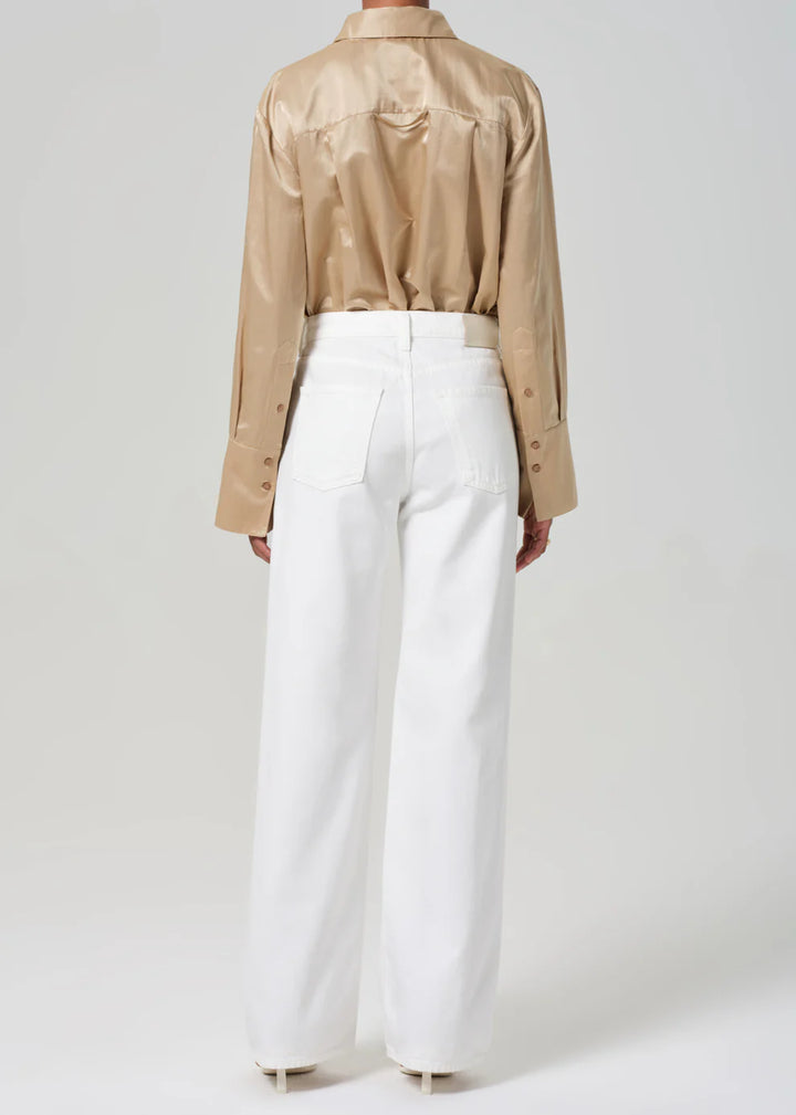 Person wearing a beige shirt and white pants on a plain background