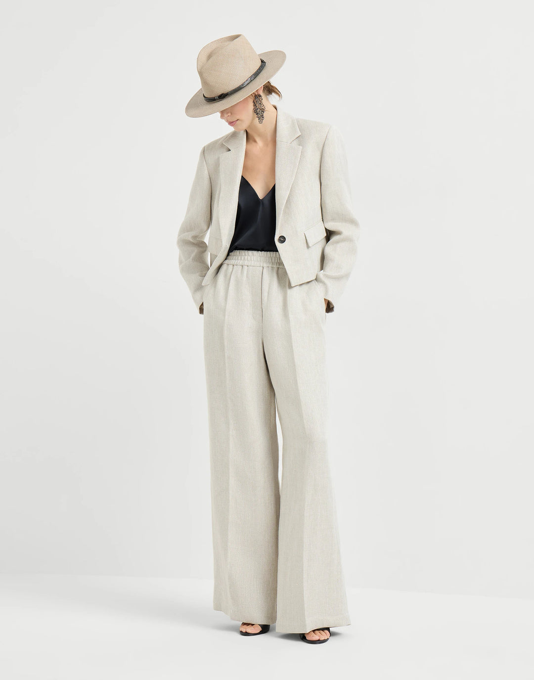 Person wearing a beige suit with wide-leg pants and a hat on a white background