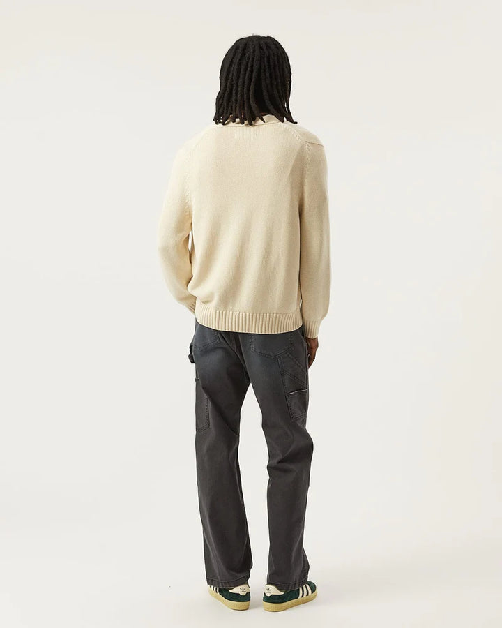 Person wearing a beige sweater and dark pants on a white background