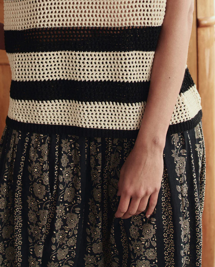 Person wearing a black and white patterned top with a black and gold floral skirt.