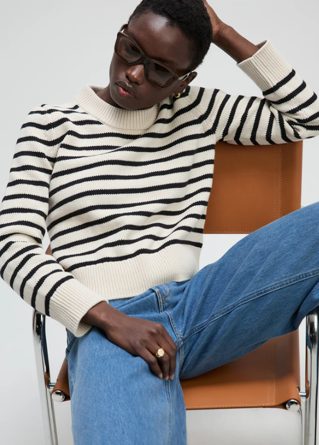 Person wearing a black and white striped sweater and blue jeans sitting on a chair.