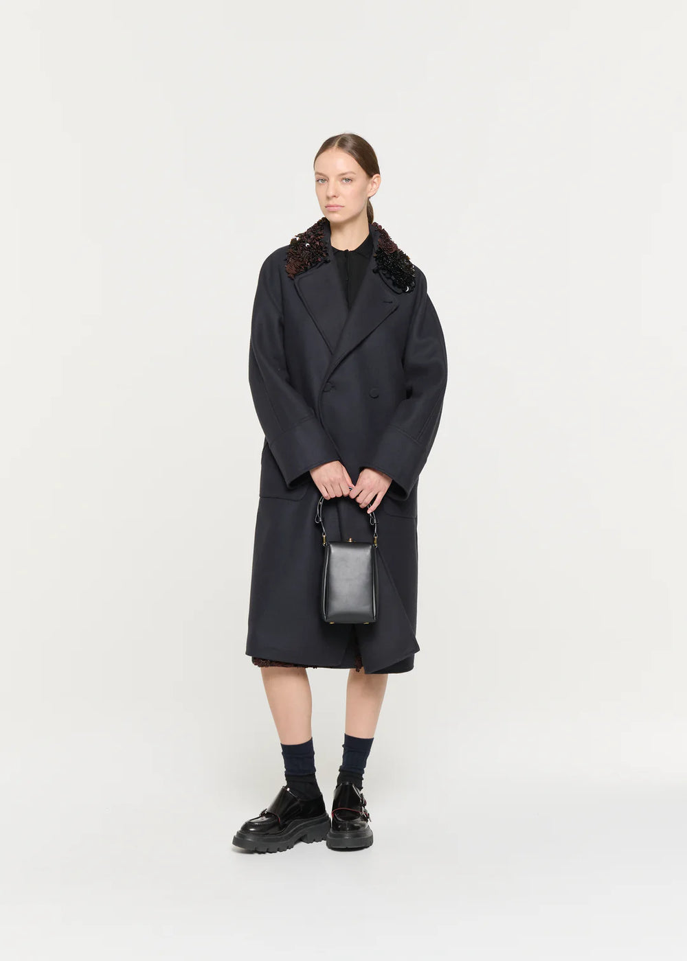 Person wearing a black coat with decorative trim on a white background