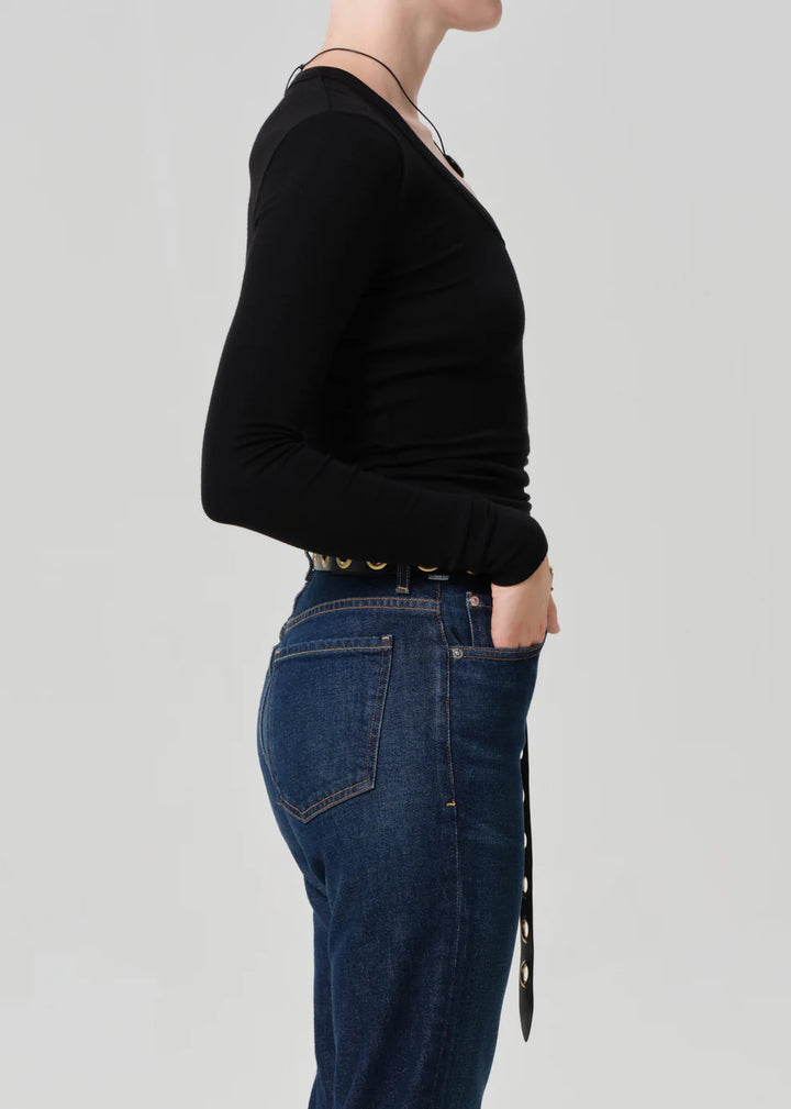 Person wearing a black long-sleeve top and blue jeans on a light gray background