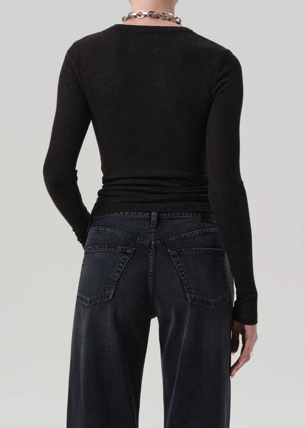 Person wearing a black long-sleeve top and dark jeans on a light gray background