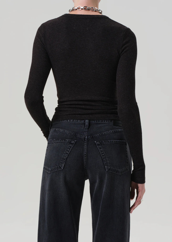 Person wearing a black long-sleeve top and dark jeans on a light gray background