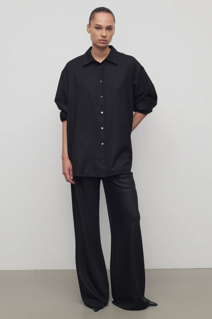 Person wearing a black outfit with wide-leg pants against a plain background