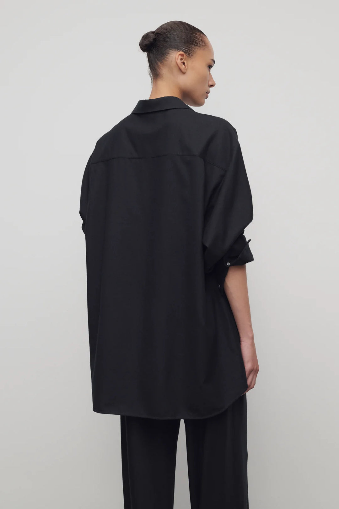 Person wearing a black oversized shirt and pants on a plain background