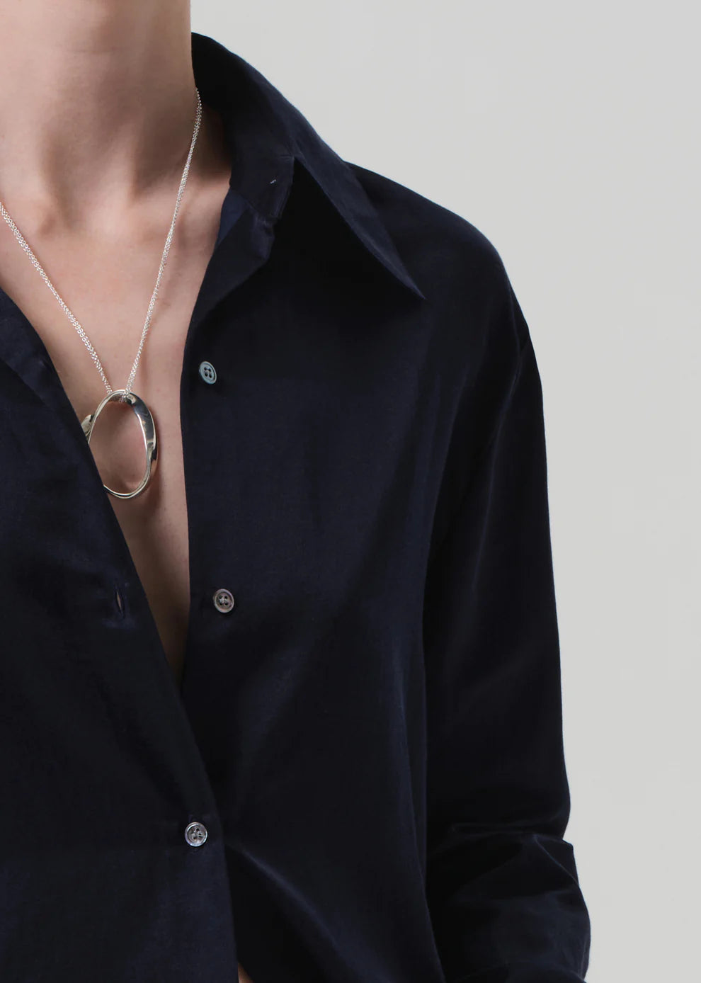 Person wearing a black shirt with a necklace featuring a large circular pendant on a plain background