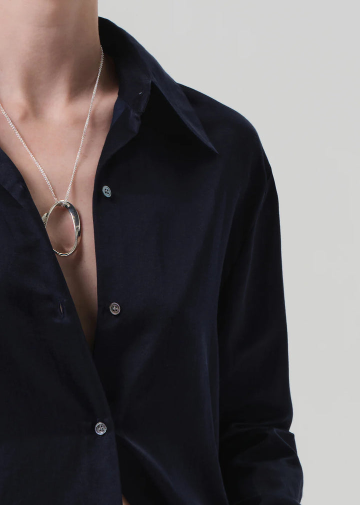 Person wearing a black shirt with a necklace featuring a large circular pendant on a plain background