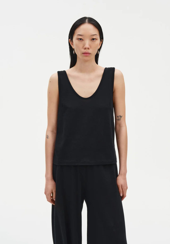 Person wearing a black sleeveless top and black pants on a white background