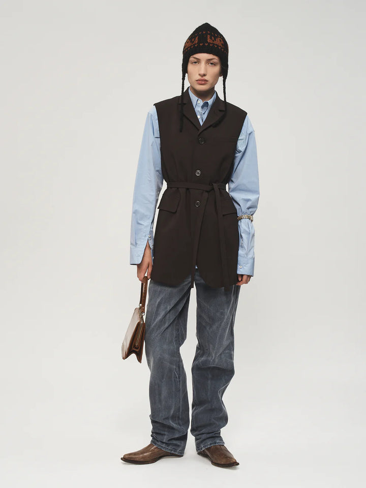 Person wearing a black vest, light blue shirt, gray pants, and brown shoes on a white background