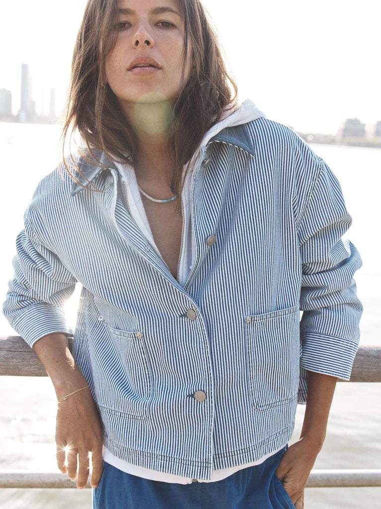 Person wearing a blue and white striped jacket with a blurred cityscape in the background