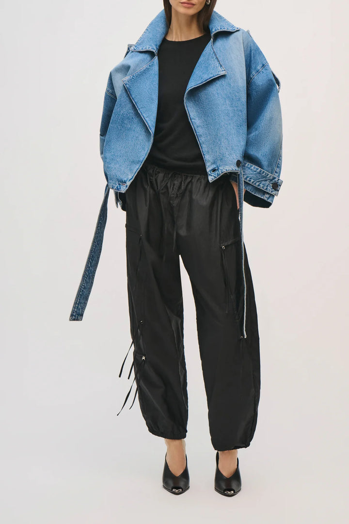 Person wearing a blue denim jacket and black pants on a white background