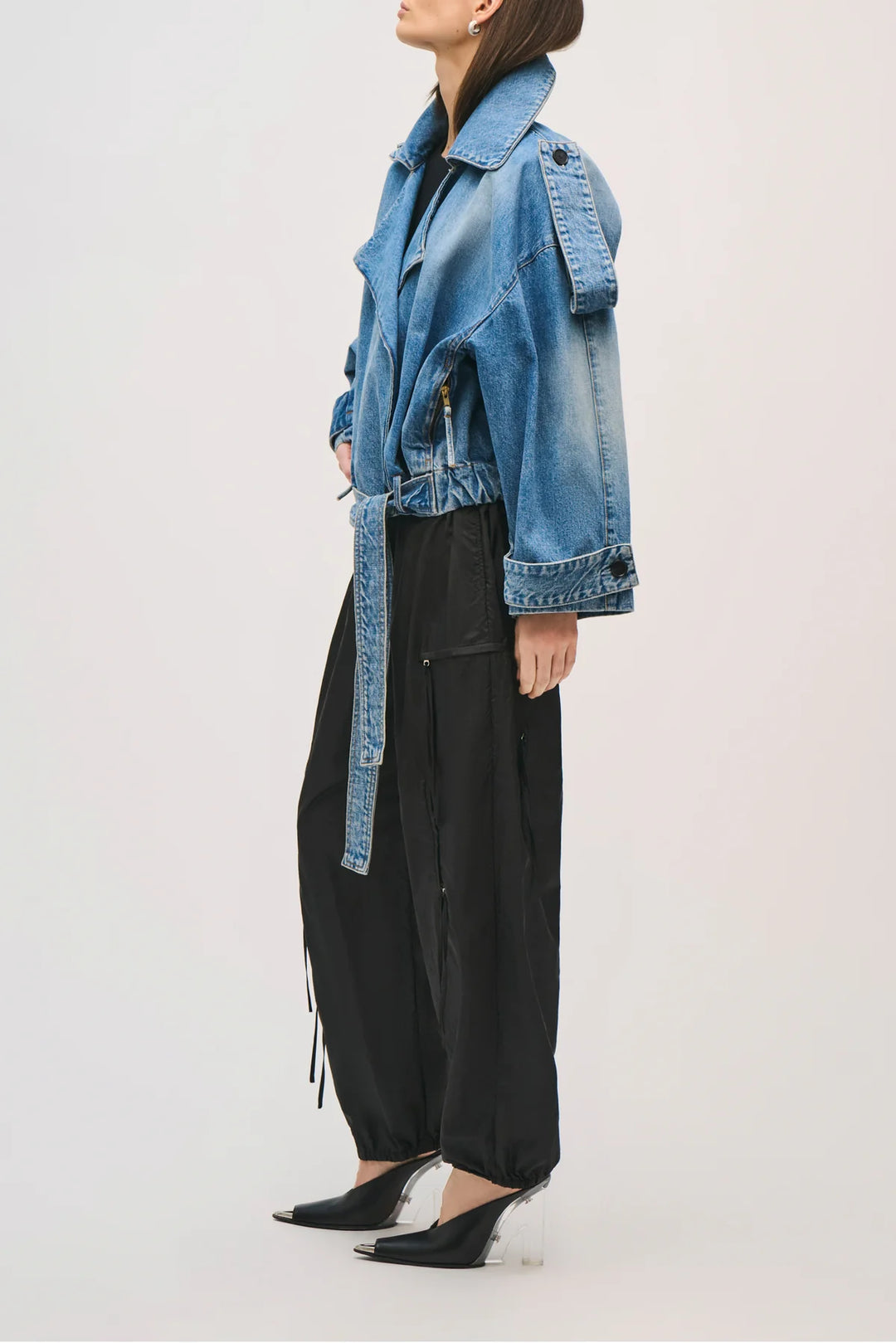 Person wearing a blue denim jacket over a black outfit on a white background