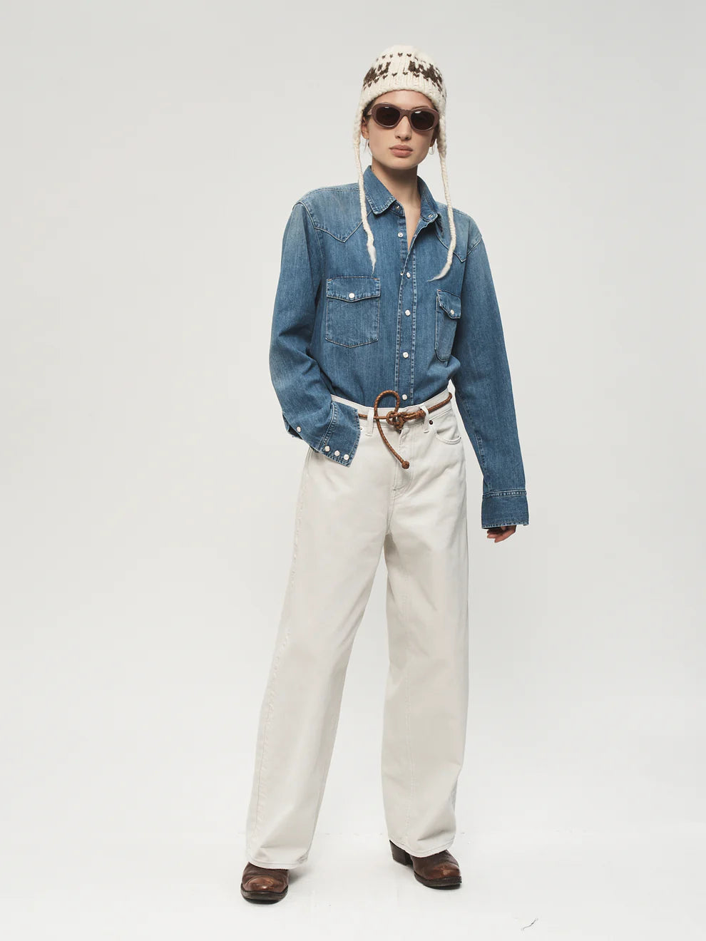 Person wearing a blue denim jacket, white pants, and a patterned beanie on a plain background