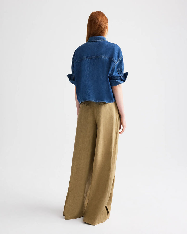 Person wearing a blue denim shirt and brown wide-leg pants on a white background