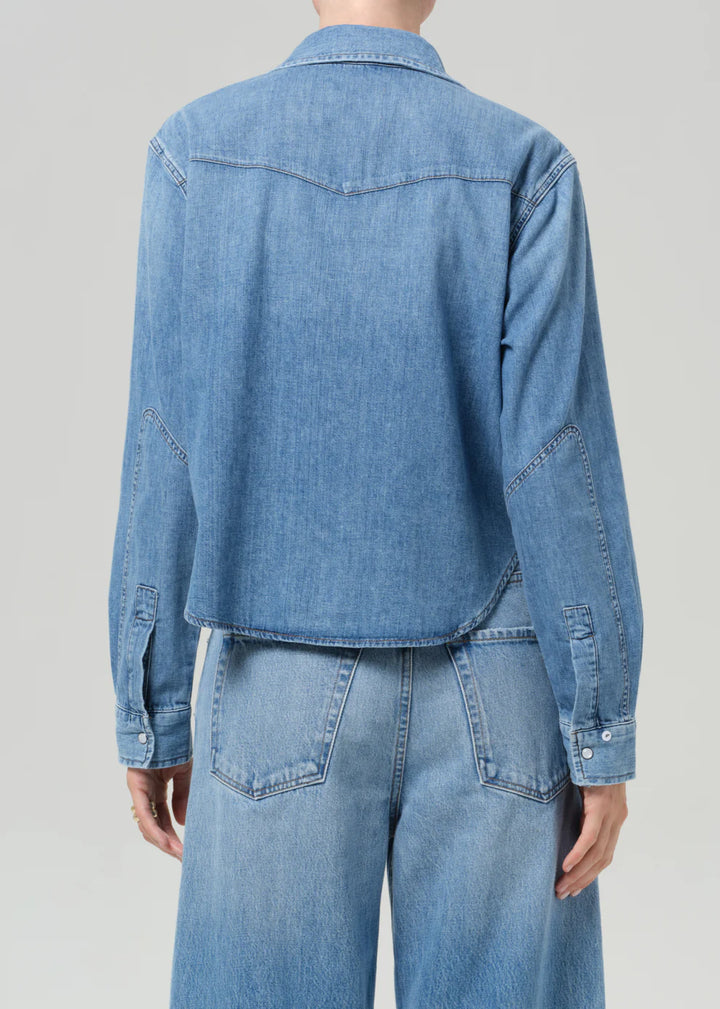 Person wearing a blue denim shirt and jeans on a gray background