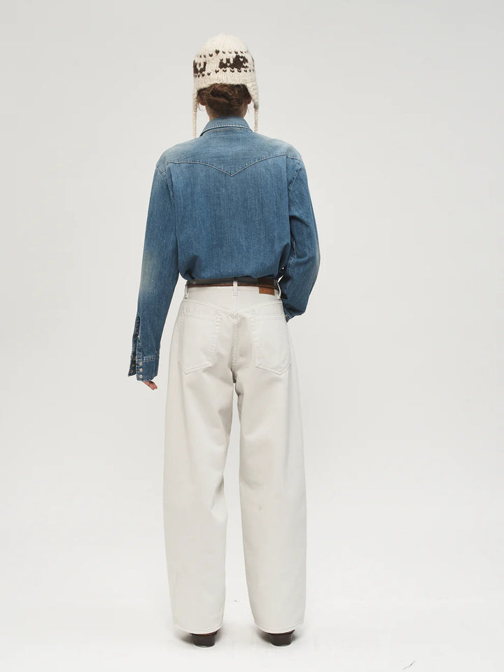 Person wearing a blue denim shirt and white pants on a plain background