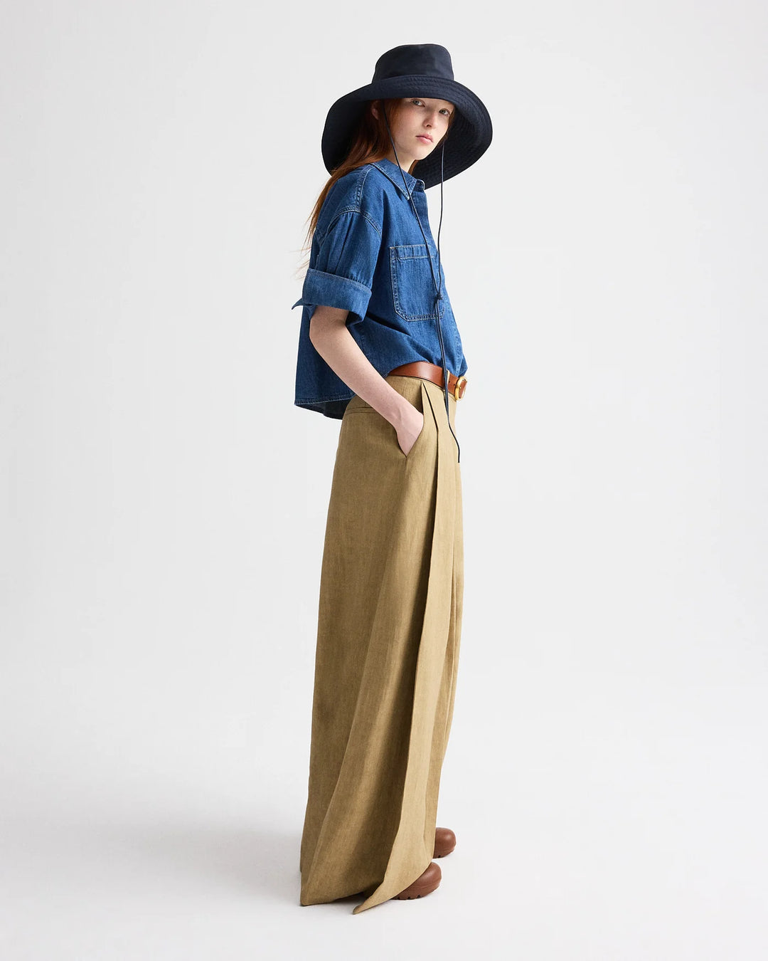 Person wearing a blue denim shirt and wide-leg beige pants with a black hat on a white background