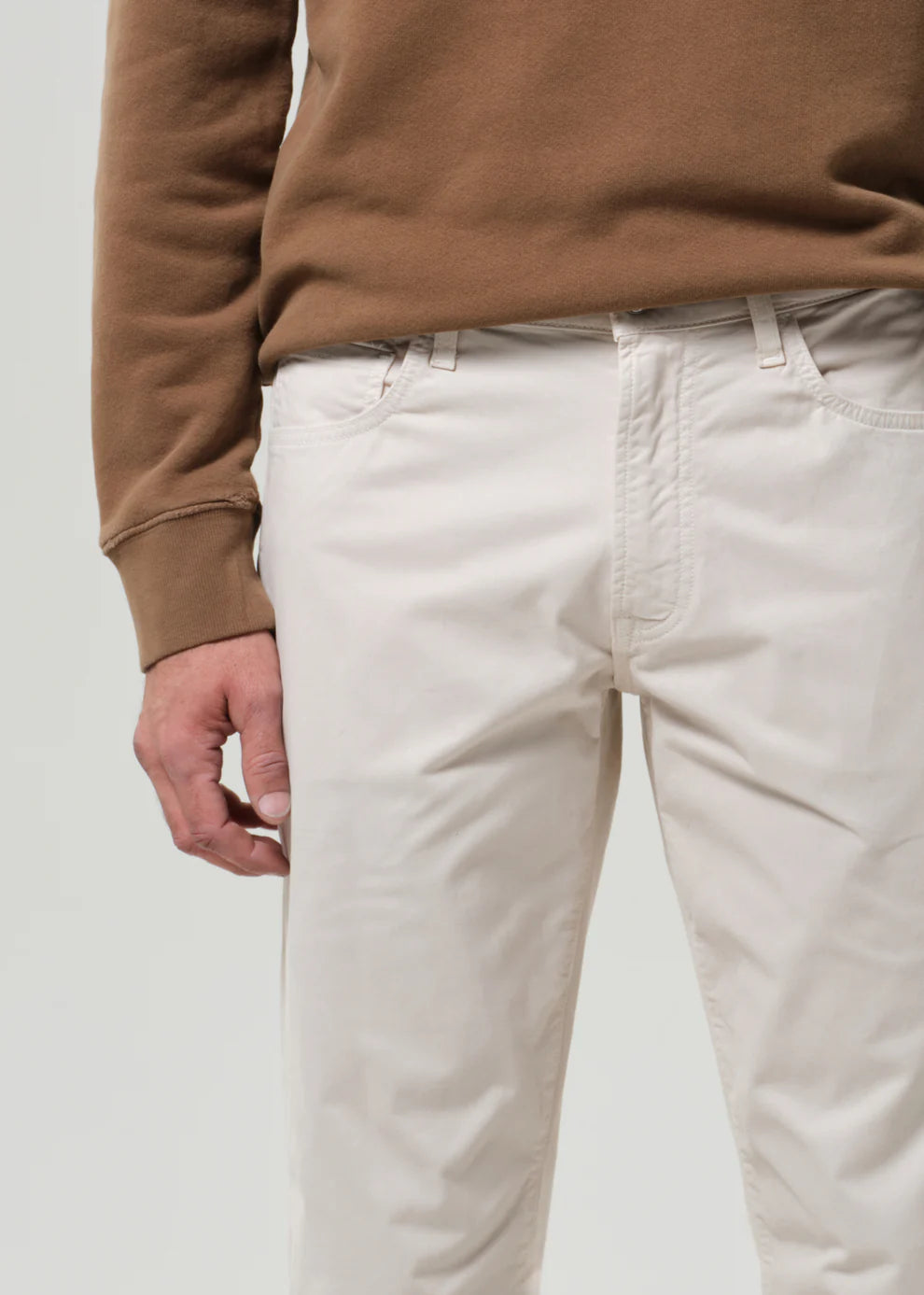 Person wearing a brown sweater and white pants on a plain background