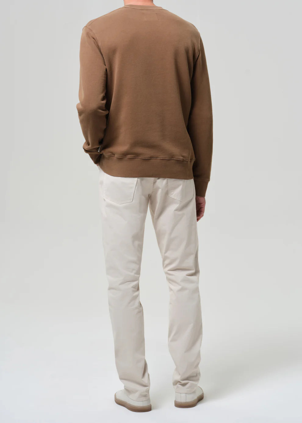 Person wearing a brown sweatshirt and beige pants on a white background