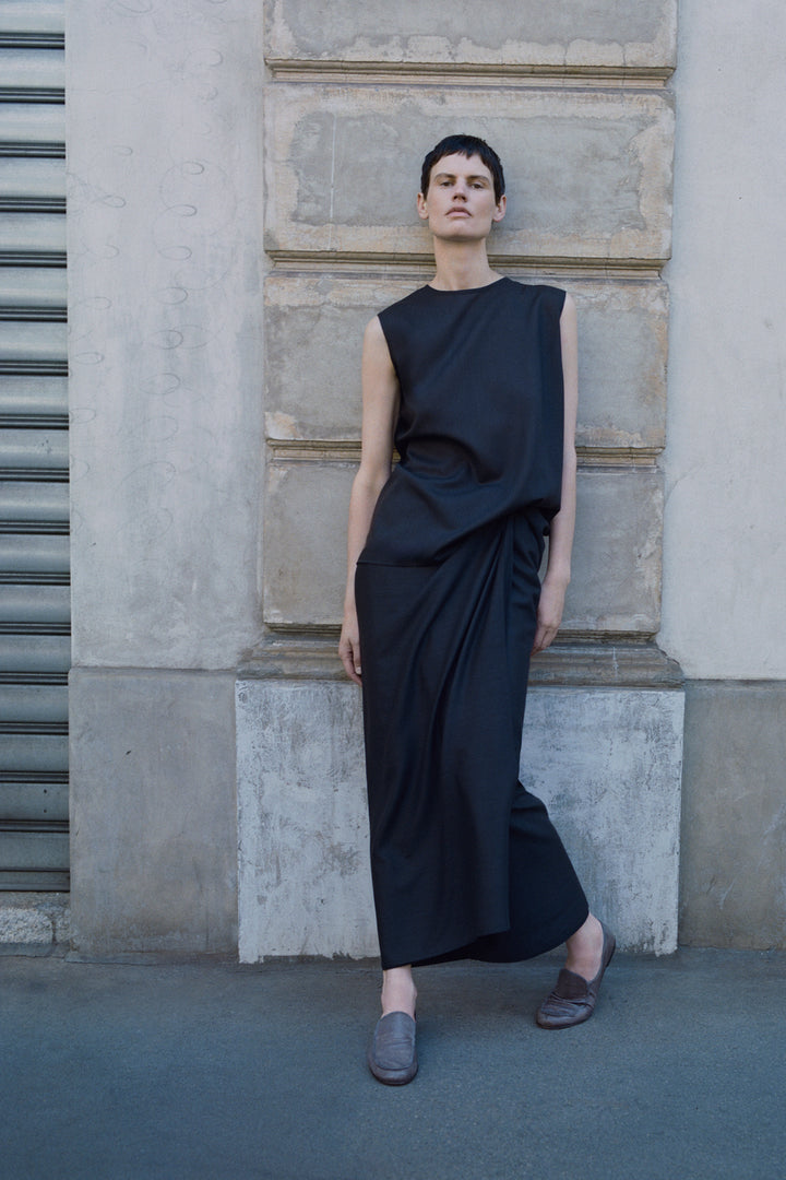 Person wearing a dark blue sleeveless dress standing against a textured wall.