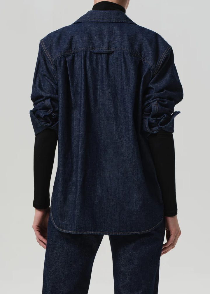 Person wearing a dark denim jacket on a plain background