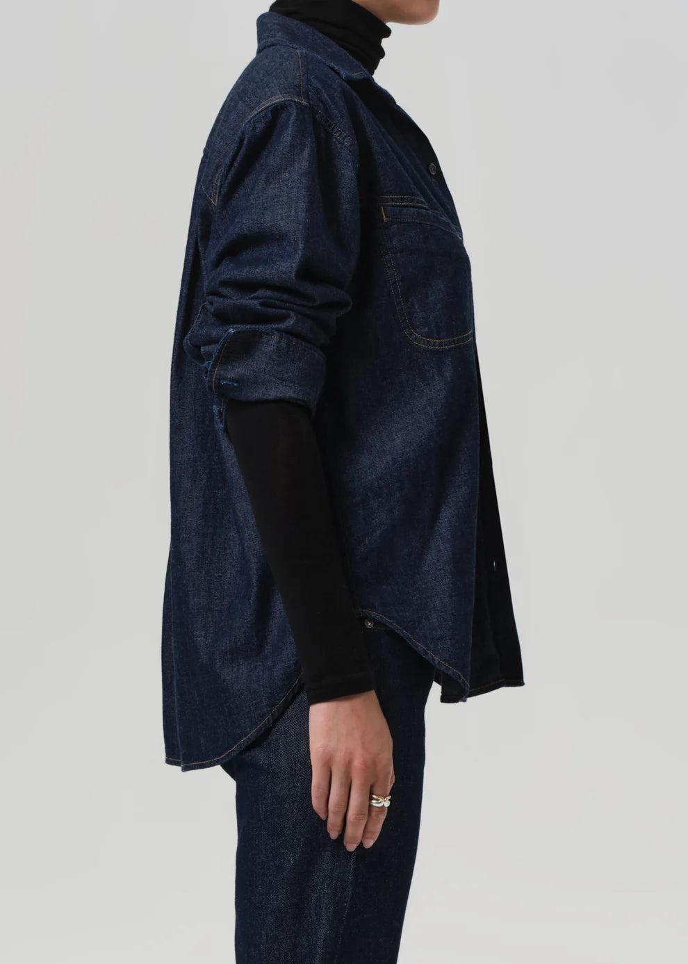 Person wearing a dark denim jacket over a black turtleneck on a plain background