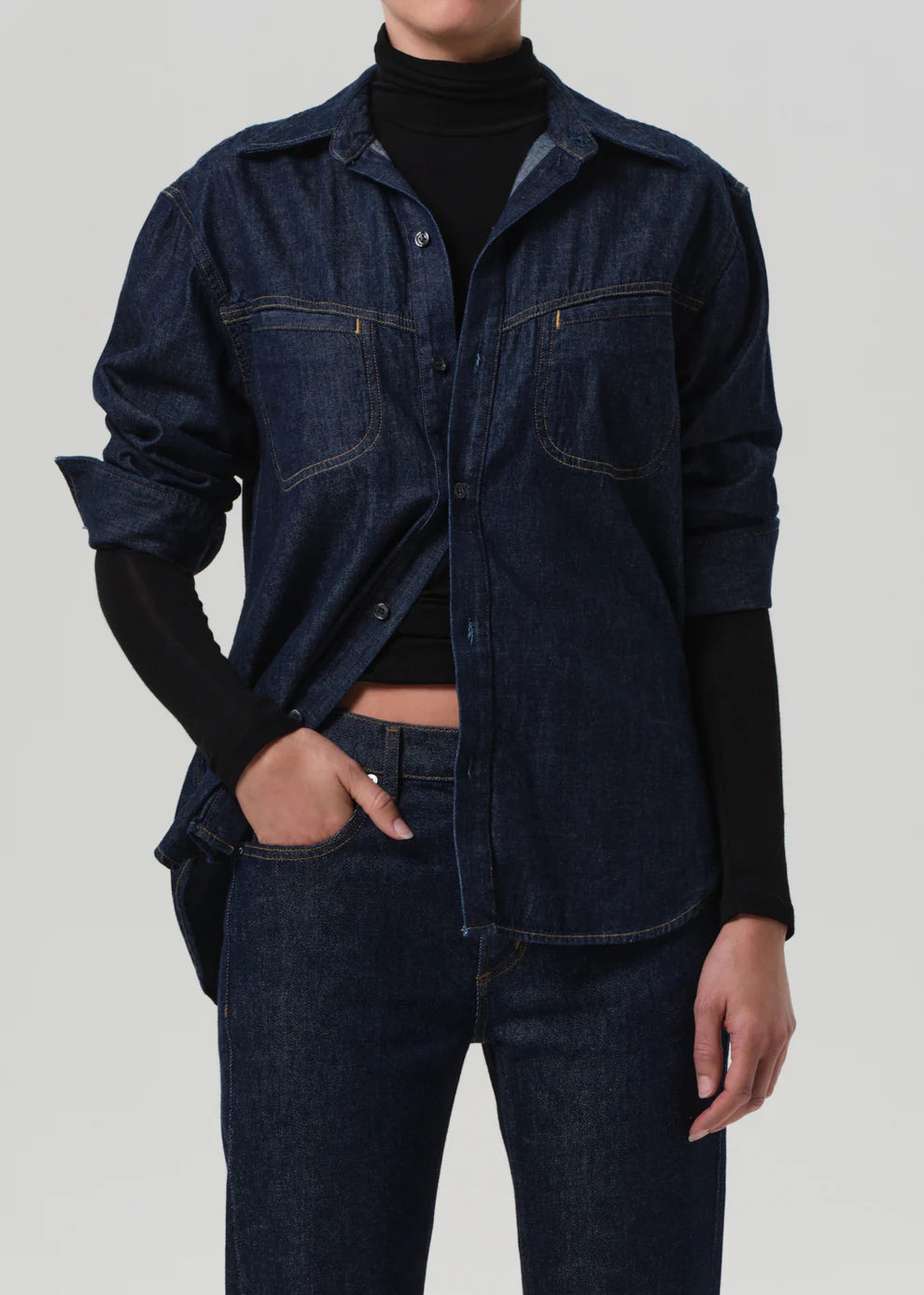 Person wearing a dark denim shirt and jeans on a plain background