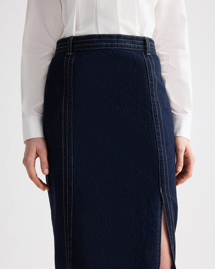 Person wearing a dark denim skirt with a white shirt on a light background